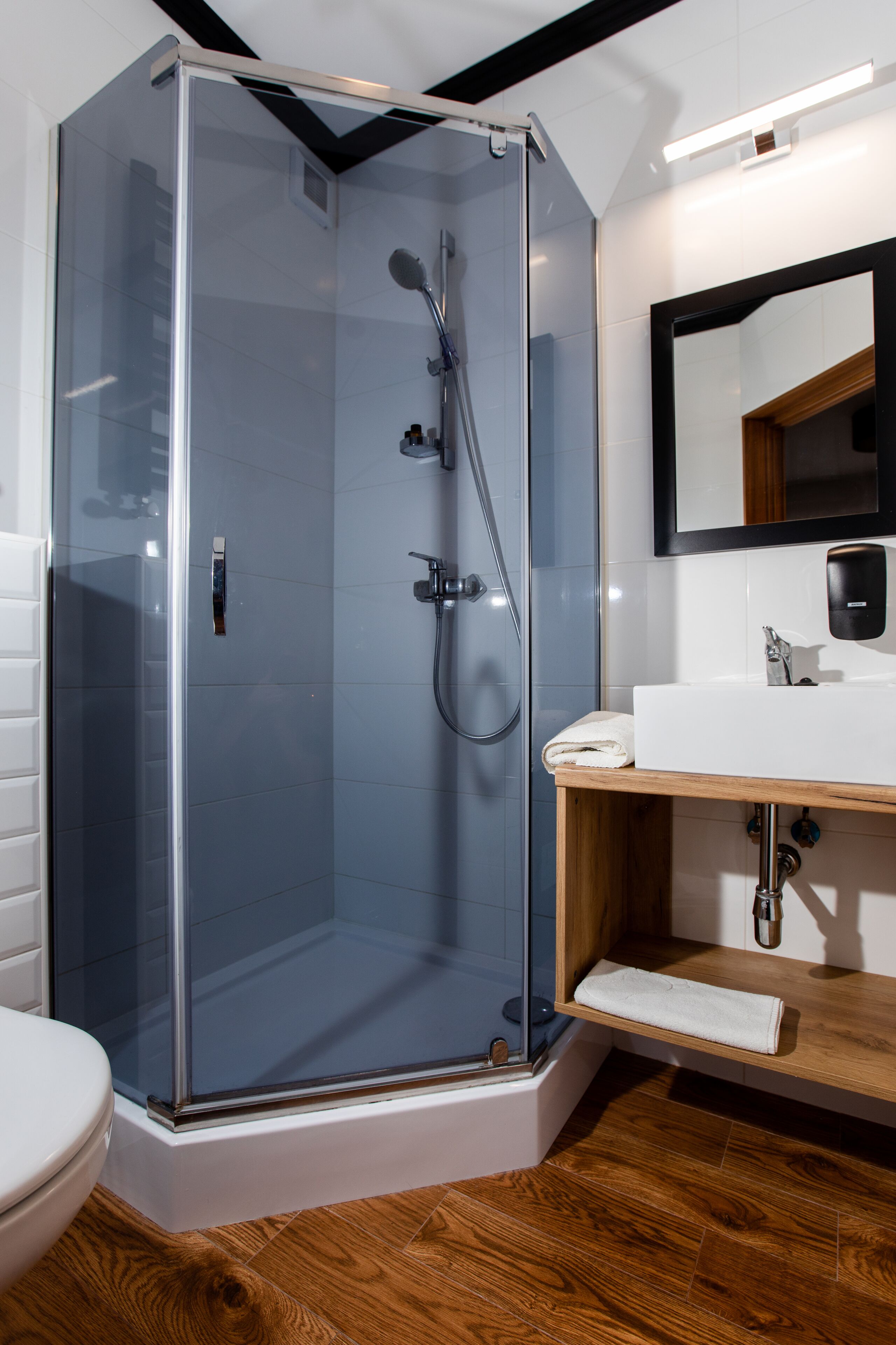 Un bagno moderno con cabina doccia in vetro, lavandino bianco e mobile contenitore in legno.