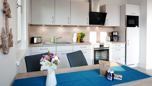 Una cocina moderna con armarios blancos, un tostador de acero inoxidable, un lavamanos, un microondas y un horno. Hay un mantel azul sobre la mesa con un jarrón de flores.