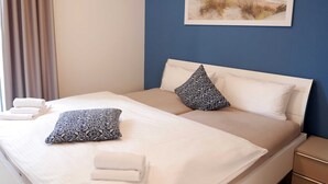 Una cama bien hecha con dos almohadas, una toalla doblada y un cuadro con una playa en la pared.
