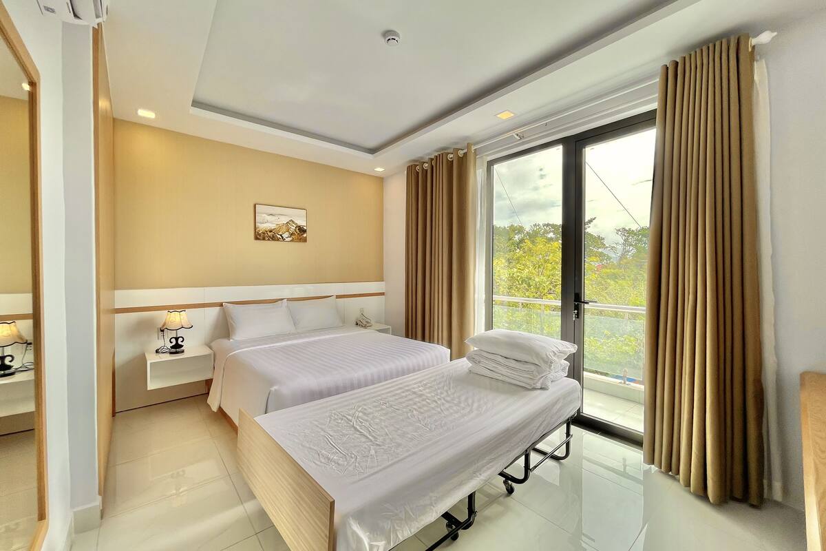 Una habitación de hotel moderna con una cama grande, mesitas de noche, un velador, una ventana con cortinas y vistas a zonas verdes.
