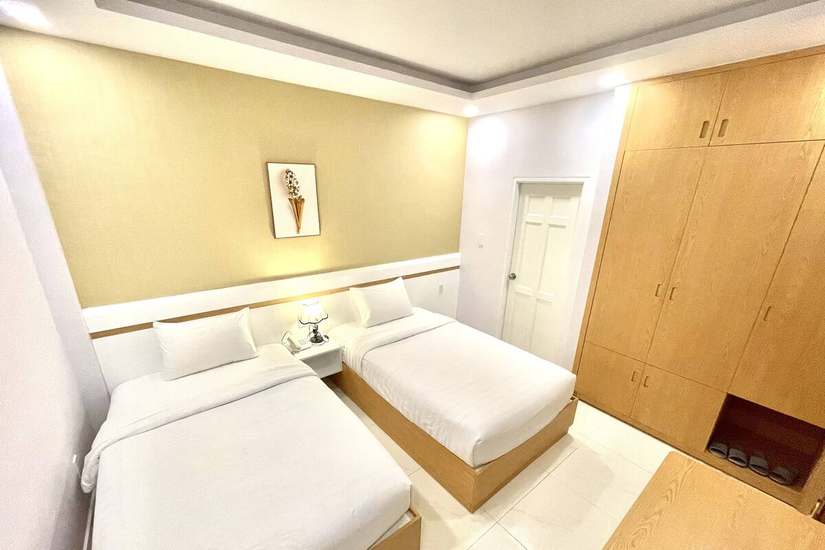 Una habitación de hotel con dos camas, una mesita de noche con lámpara, una obra de arte en la pared y un armario de madera.