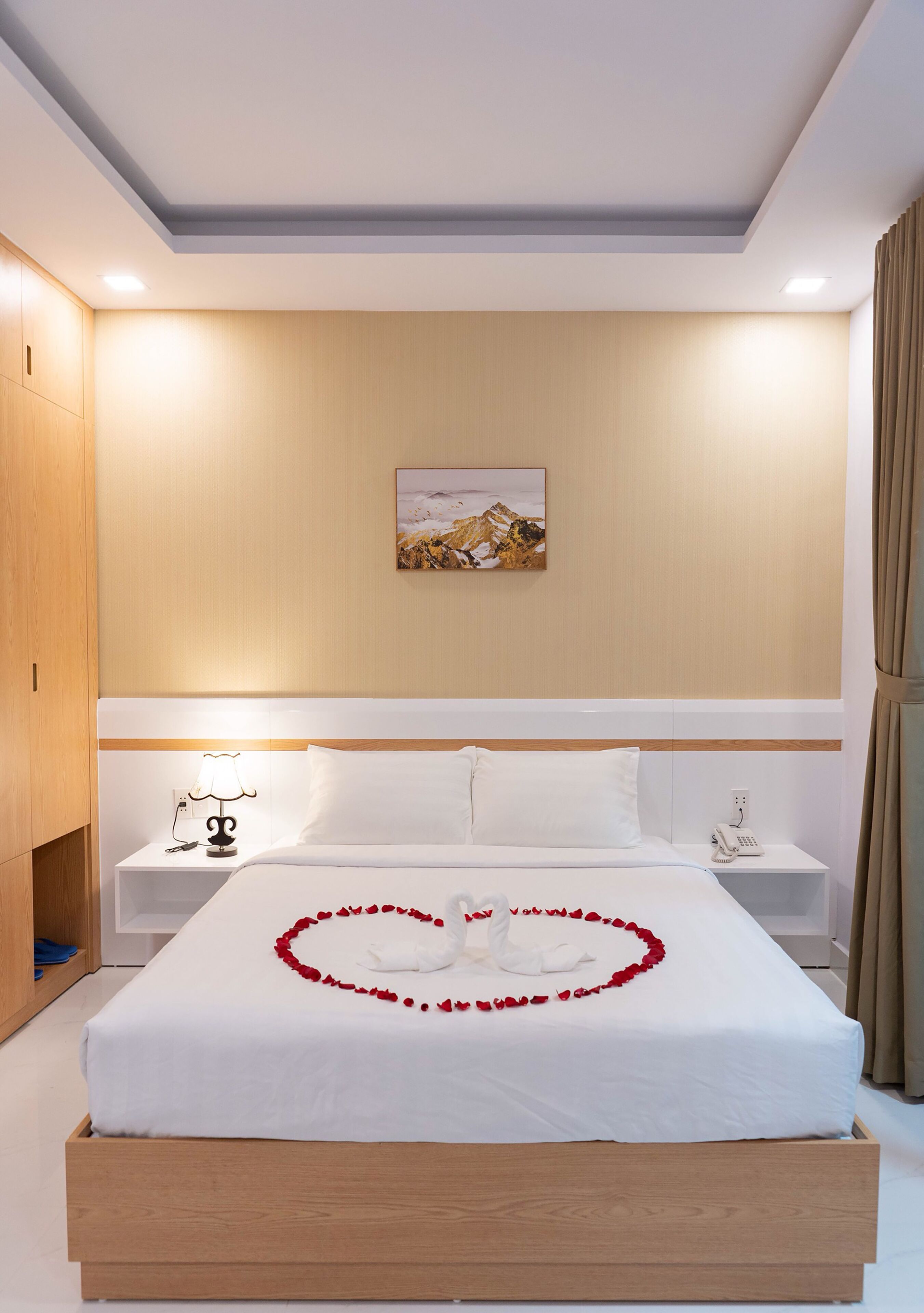A neatly made bed with white linens, a heart-shaped rose decoration, and a painting on the wall.