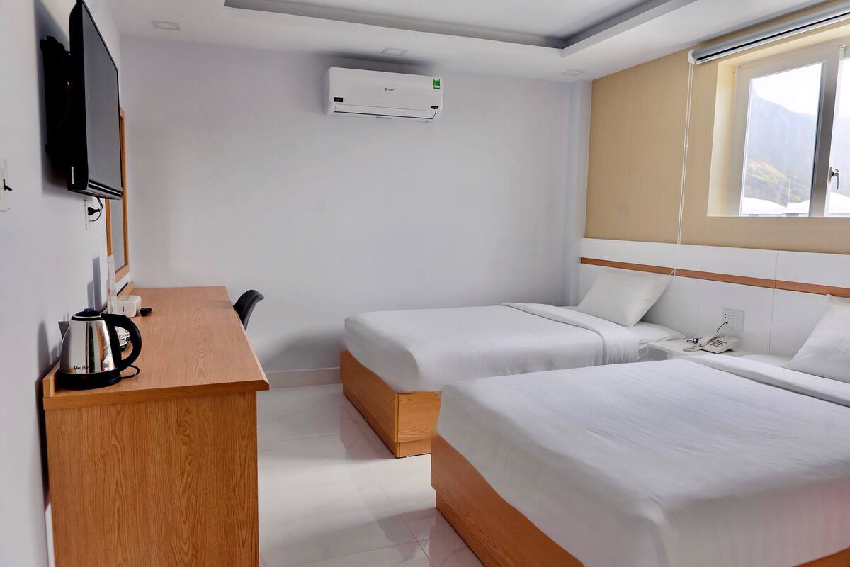 Habitación de hotel con dos camas individuales, un escritorio de madera con hervidor, un televisor de pantalla plana y un equipo de aire acondicionado.