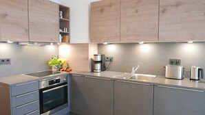 A modern kitchen with stainless steel appliances, wooden cabinets, and a built-in oven. - Baabe Villen Ensemble FeWo 03 Ahoi Ref. 211406 (Baabe)