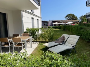 Um pátio com mesa e cadeiras de jantar, uma poltrona de descanso e um jardim bem cuidado, com sebes e gramado.
