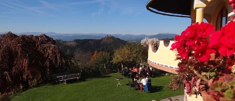 A terrace with a view of mountains, a dining area with people, and a building with a curved roof.