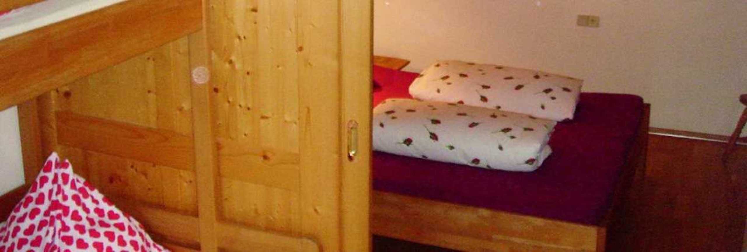 Un lit superposé en bois avec un matelas rouge et une literie blanche à motifs.