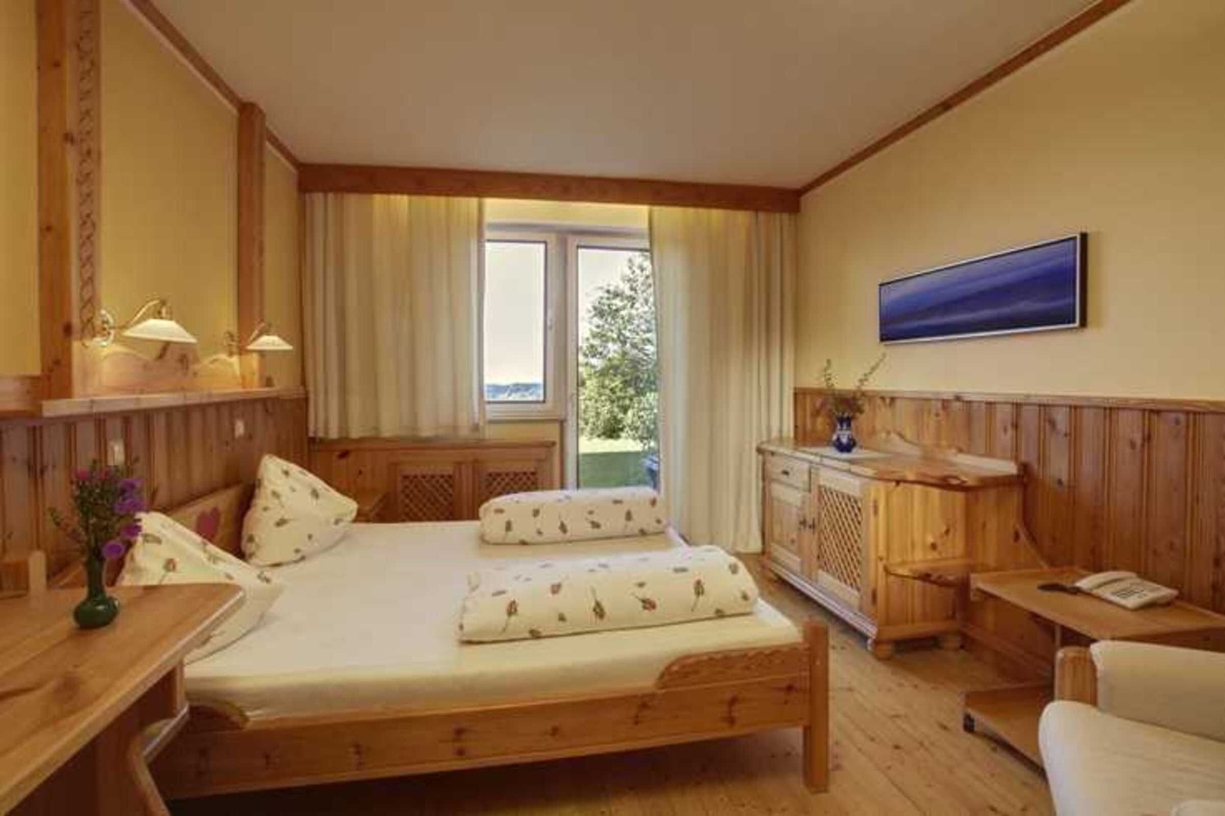 A wooden room with a bed, bedside table, lamp, and a window with curtains.