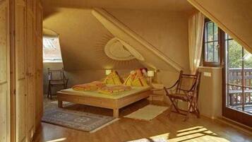Ein Schlafzimmer mit schrägem Dach, einem Bett, einem Sessel und einem Fenster.
