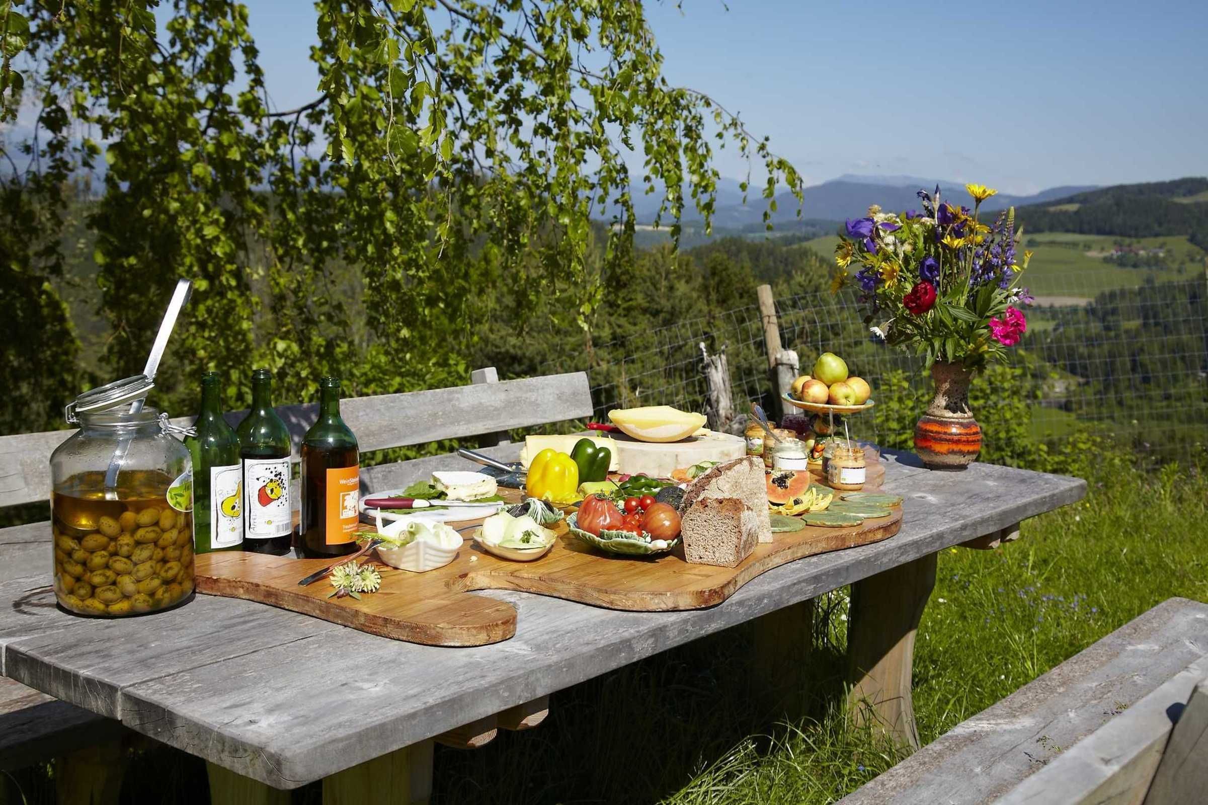 A picnic table with food, drinks, and a vase of flowers.