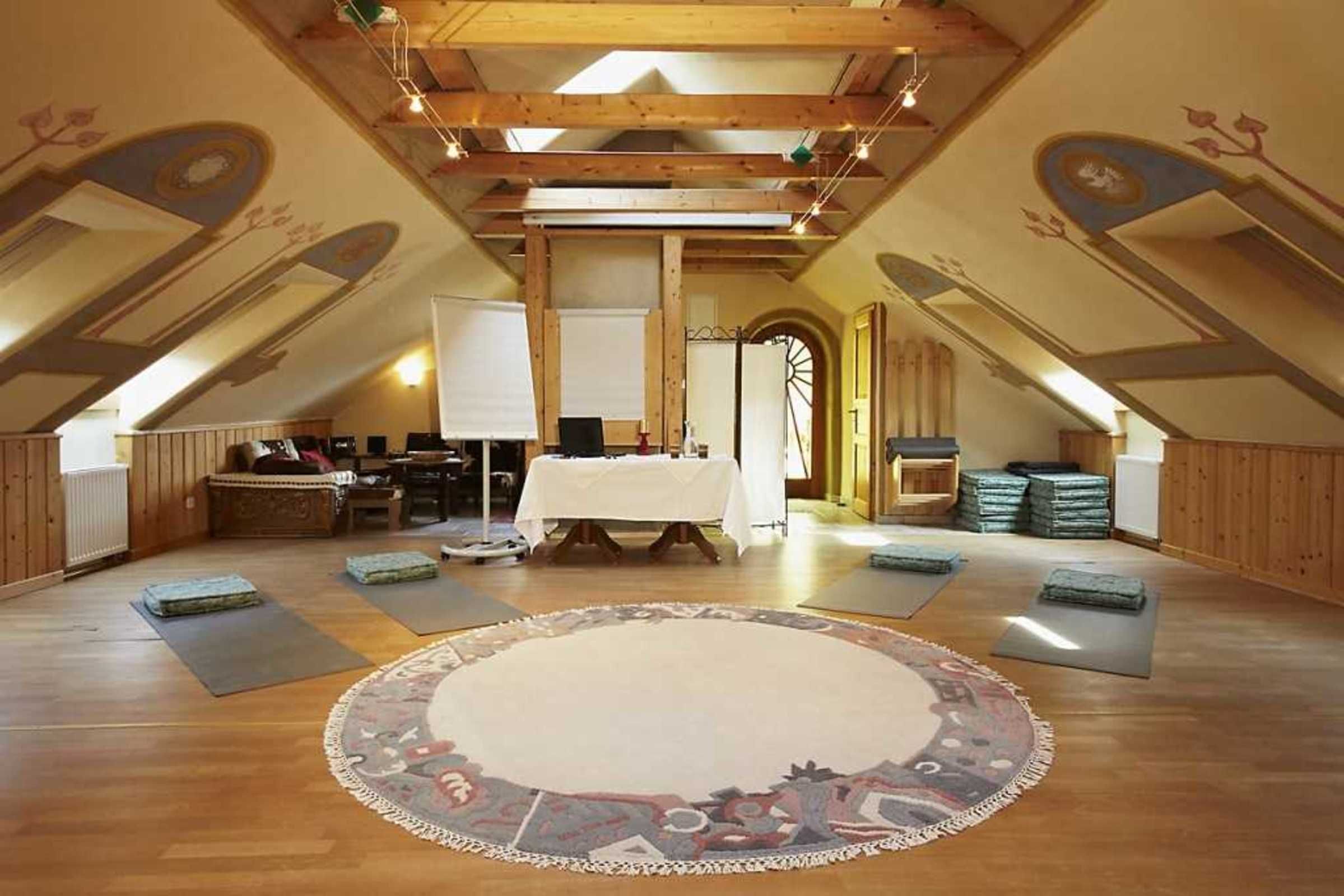 Une pièce mansardée spacieuse avec des poutres apparentes, un grand tapis rond et une table mise pour le repas.