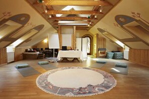 Amplia habitación en el ático con vigas de madera, un tapete redondo grande y una mesa lista para una comida.