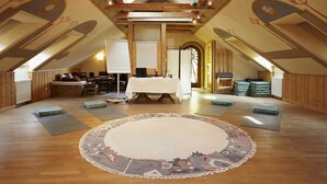 Amplia habitación en el ático con vigas de madera, un tapete redondo grande y una mesa lista para una comida.