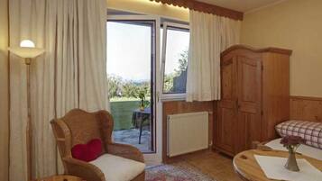 A room with a wicker chair, a wooden cabinet, a table with a vase, and a view through a glass door.