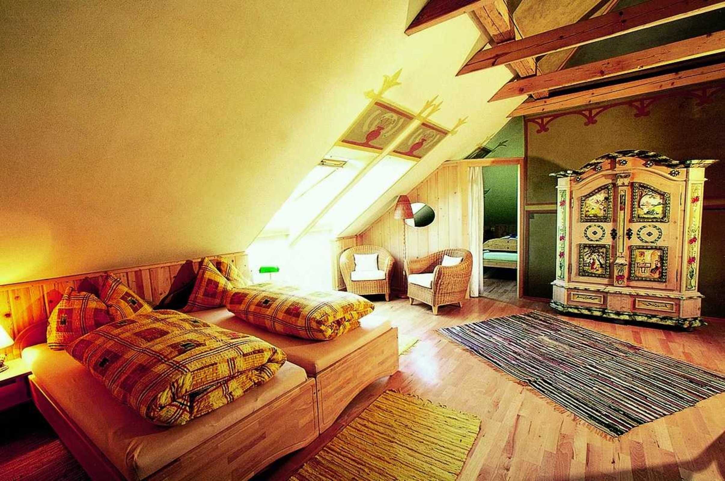 Een knus slaapkamer onder het dak, met een schuine plafond, een houten bed, een rieten stoel, een kast met ingewikkelde details, en een dakraam.