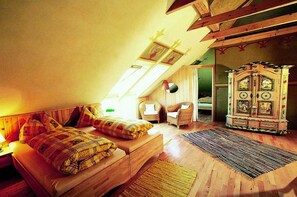 A cozy attic bedroom with a sloped ceiling, a wooden bed, a wicker chair, a cabinet with intricate designs, and a skylight. - Bionest II earth building apartment - Biolandhaus Arche (Eberstein)