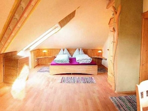 A loft bedroom with a wooden sloped ceiling, a built-in bed with pillows, and a small bedside table.