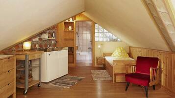 A compact attic bedroom with a kitchenette, a wooden chair, and a bed with a yellow pillow.