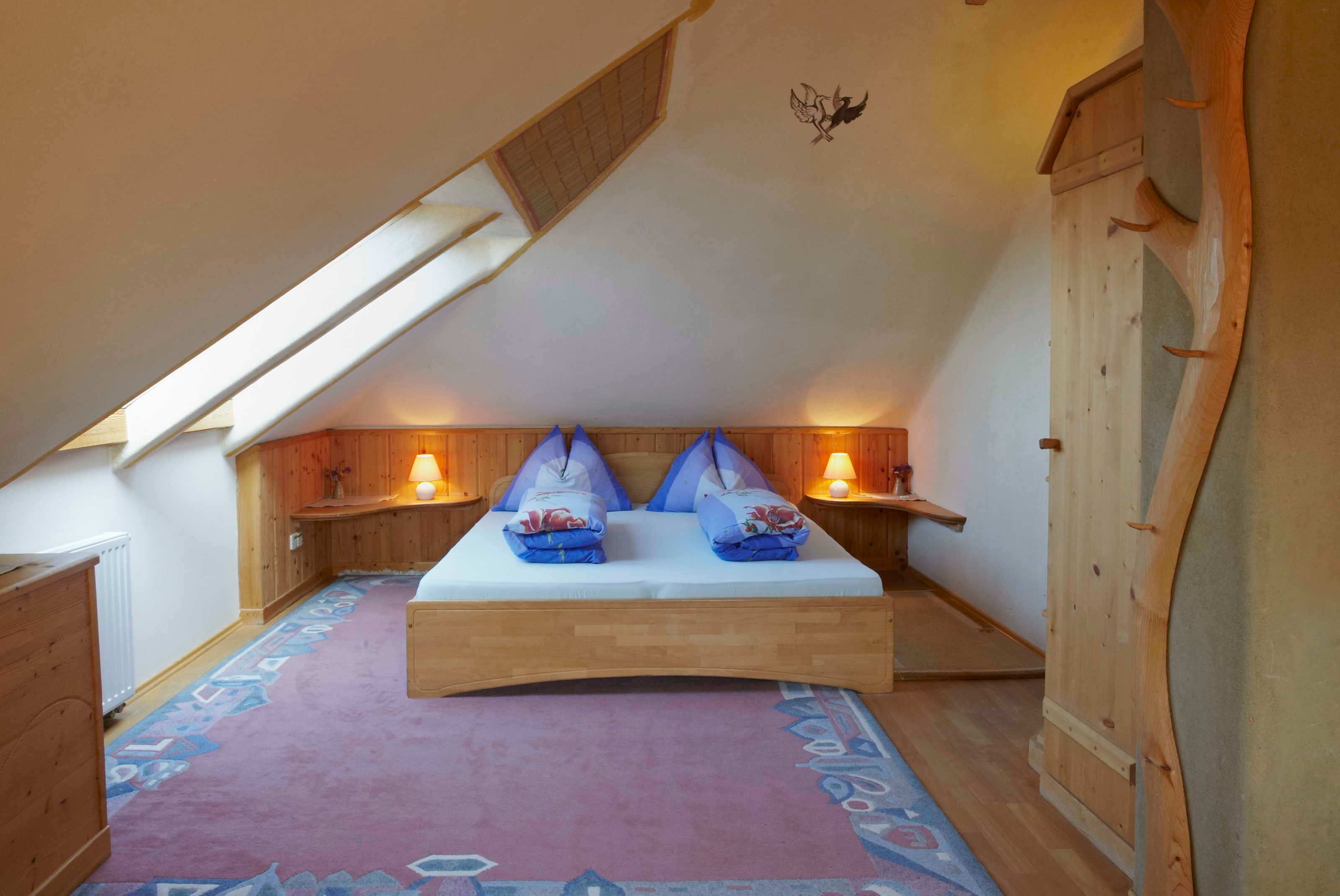 Une chambre avec un plafond en pente, des murs en bois, un lit avec des oreillers, deux lampes de chevet et un tapis à motifs.
