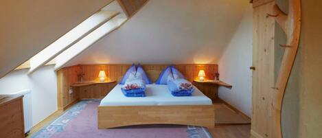 Une chambre avec un plafond en pente, des murs en bois, un lit avec des oreillers, deux lampes de chevet et un tapis à motifs.