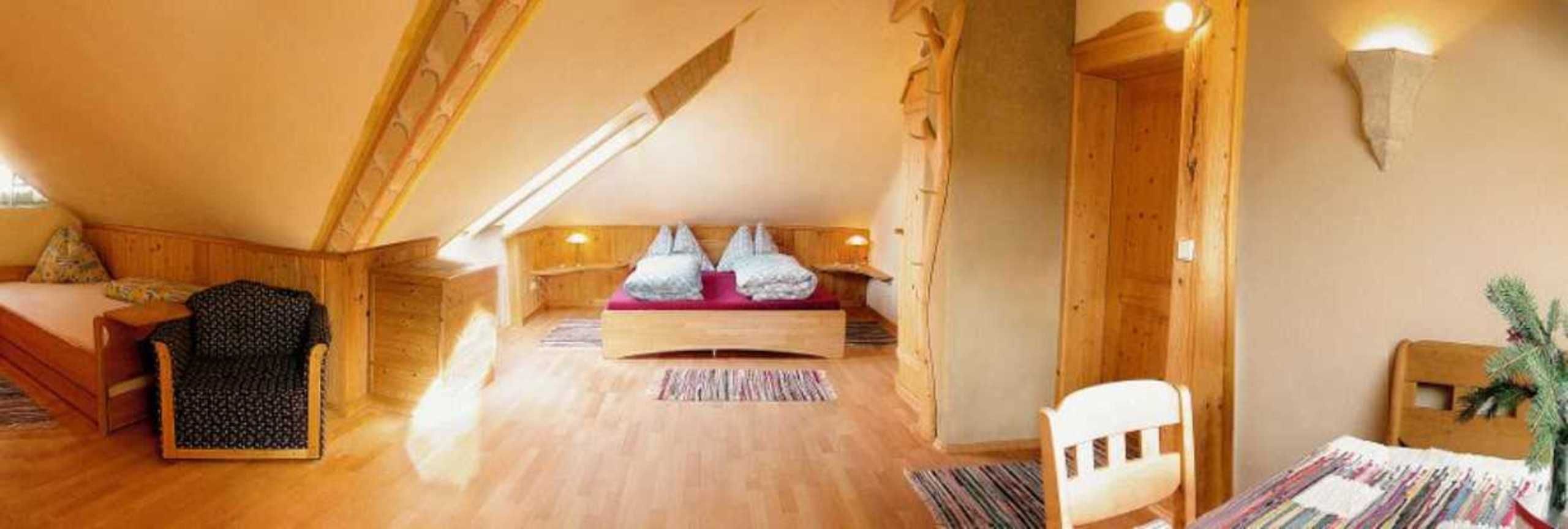 Ein gemütliches Schlafzimmer im Dachgeschoss mit Holzboden, einem Bett mit roter Matratze, einem Stuhl und einem kleinen Tisch.