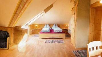 Ein gemütliches Schlafzimmer im Dachgeschoss mit Holzboden, einem Bett mit roter Matratze, einem Stuhl und einem kleinen Tisch.