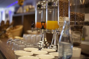 Una barra de desayuno con máquinas de café, dispensador de agua y una variedad de tazas y platos.