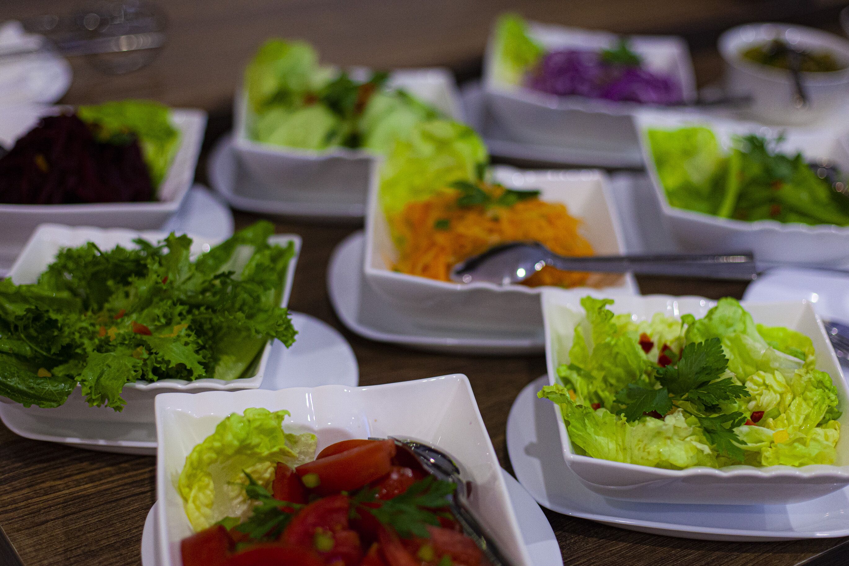Diverse salades op witte borden, gerangschikt op een houten tafel.