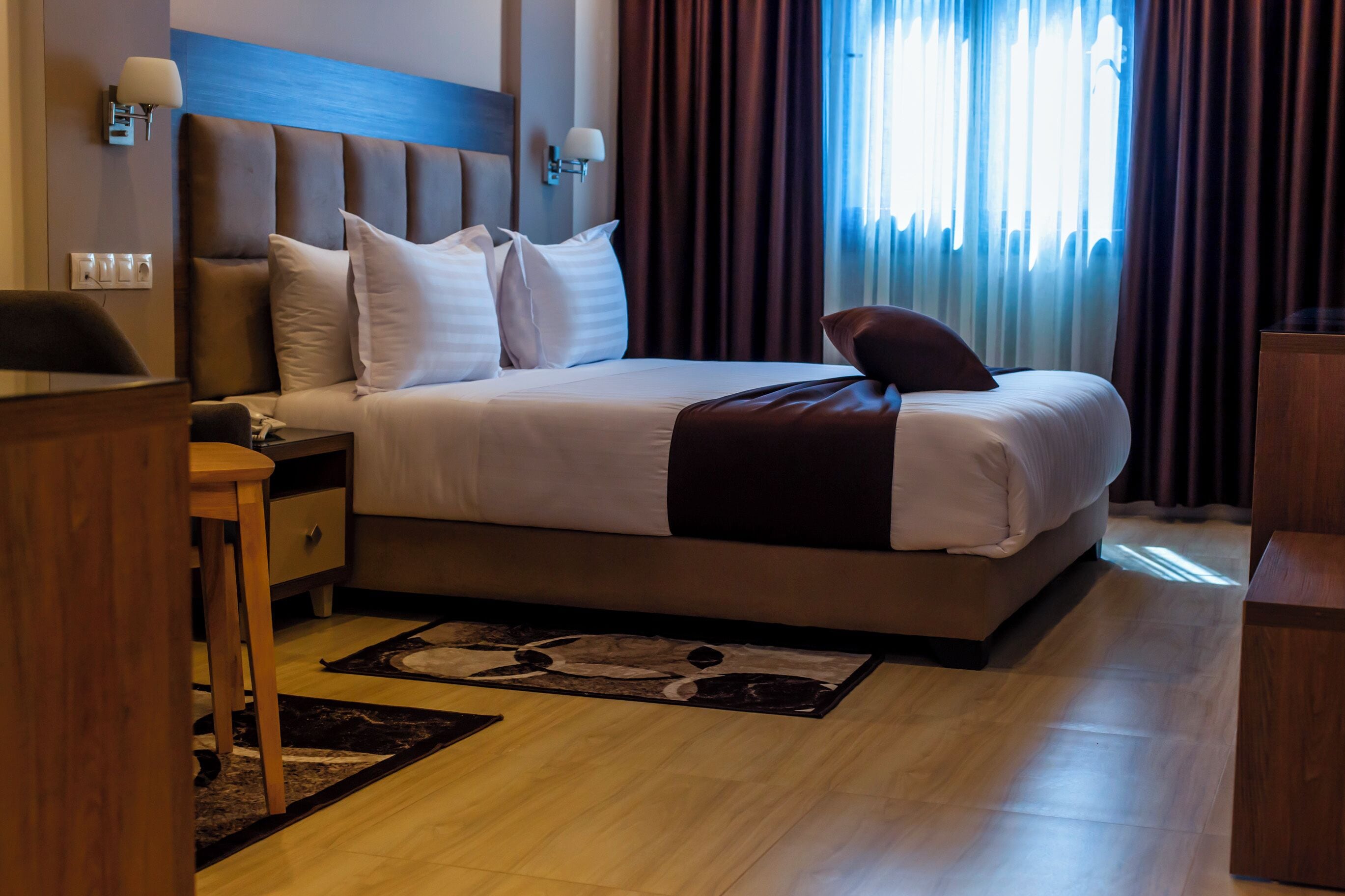 Una habitación de hotel con una cama grande, una mesita de noche de madera, un escritorio y una silla.