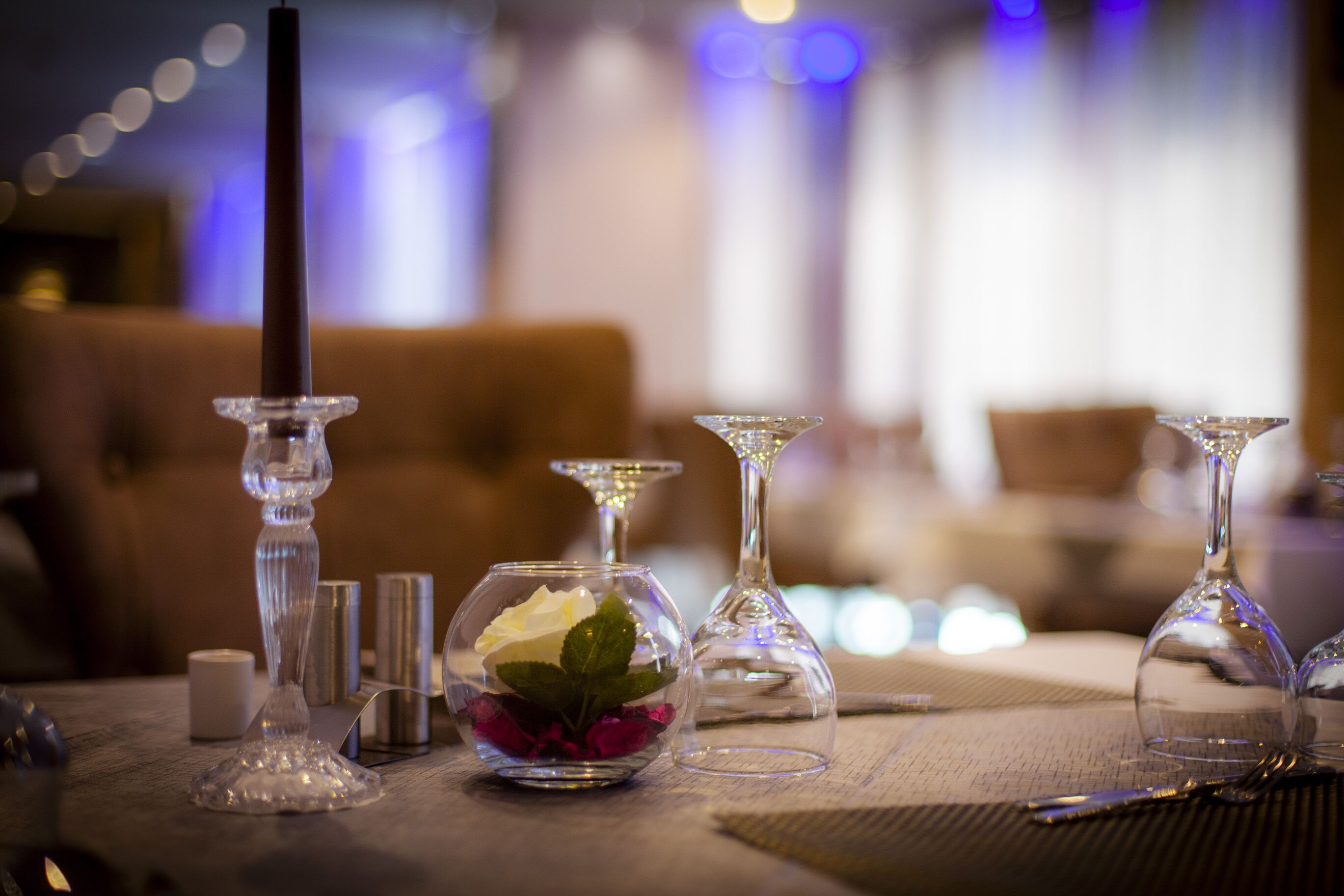 A dining table with a candle, a glass vase with a rose, and a martini glass.