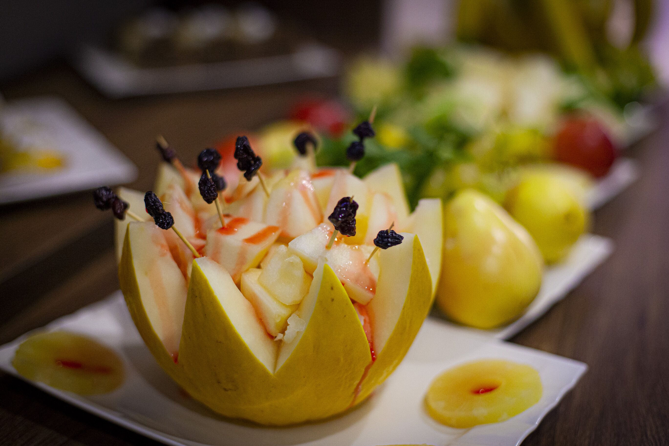Una composición de frutas en un plato, con un fondo borroso de más frutas y una mesa.