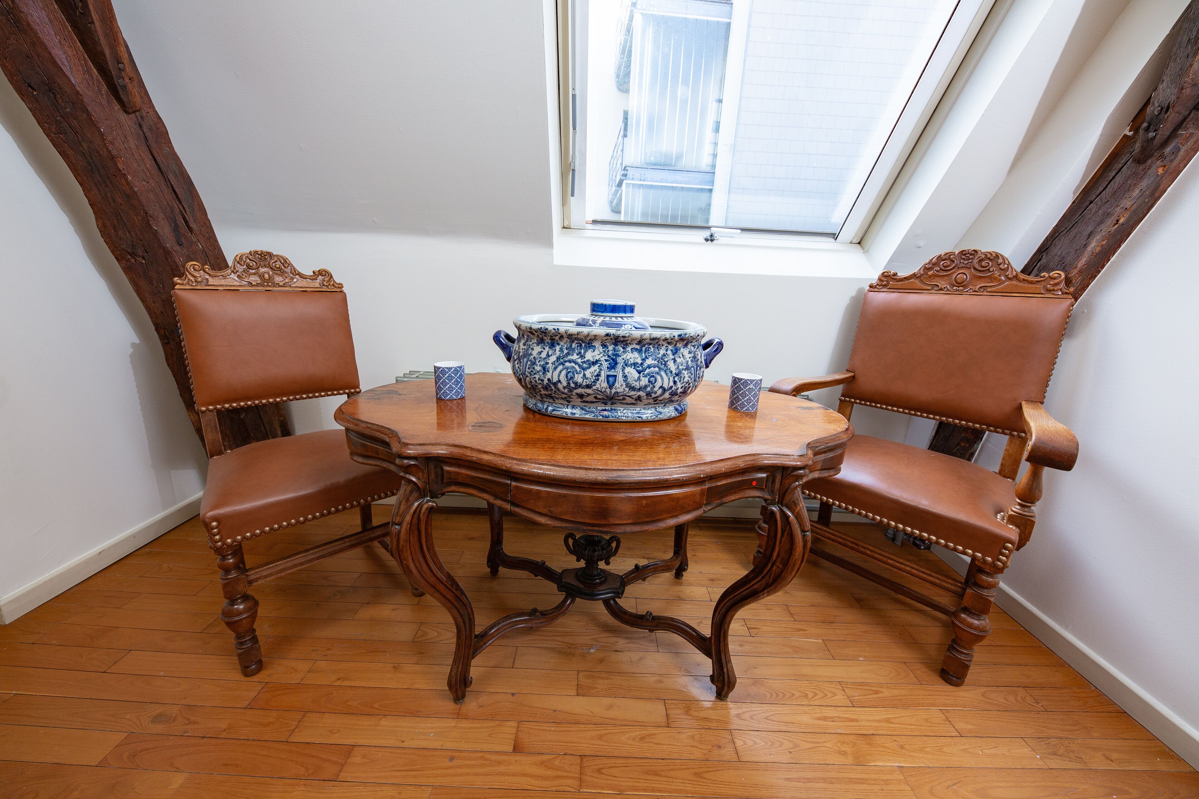 A dining table with two chairs, a blue and white ceramic bowl, and a window with blinds.