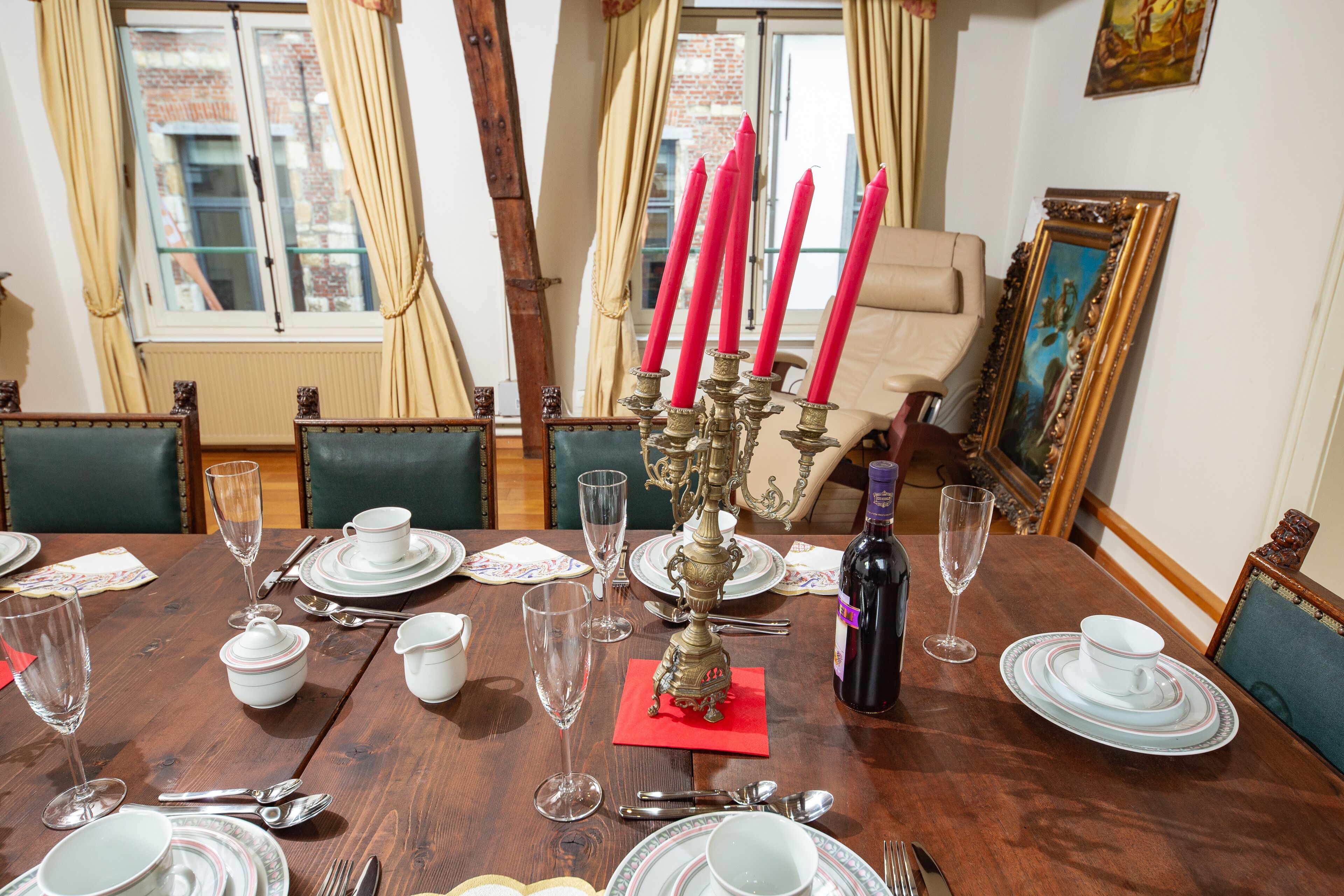 Mesa de comedor dispuesta para seis personas, con candelabro, botella de vino y diversos utensilios de mesa.