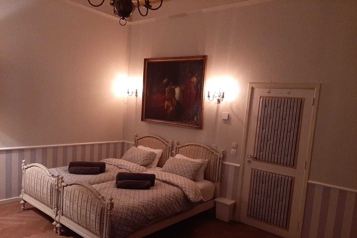 A bedroom with a four-poster bed, a painting on the wall, and a door with a window.