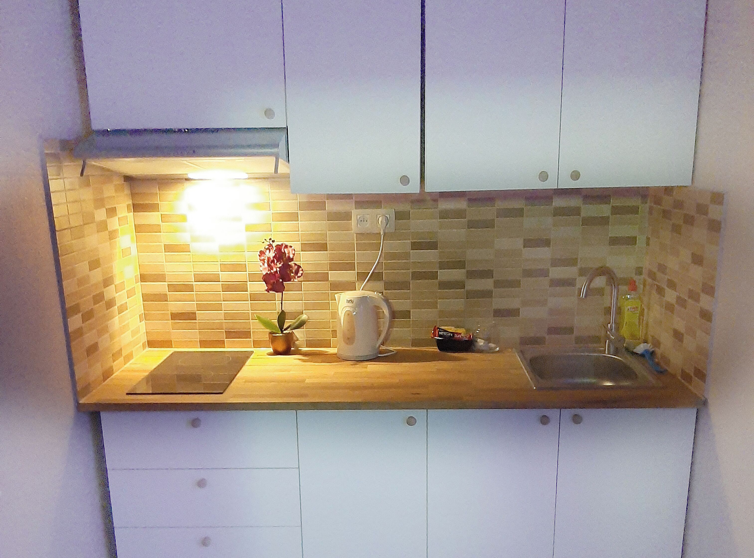 A kitchen with white cabinets, a tiled backsplash, a wooden countertop, a kettle, a sink, and a potted plant.