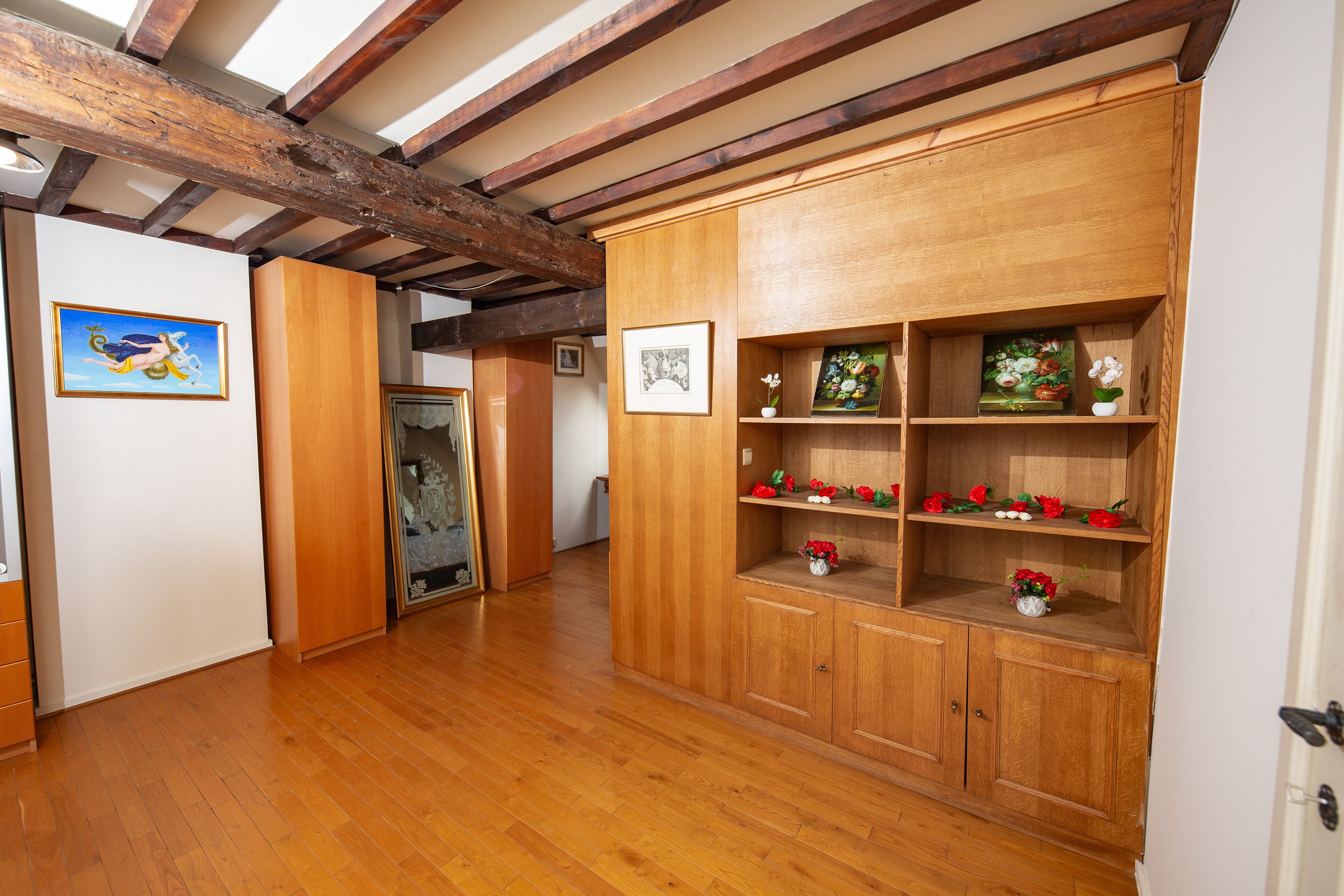 A hallway with wooden flooring and a wooden cabinet with shelves.