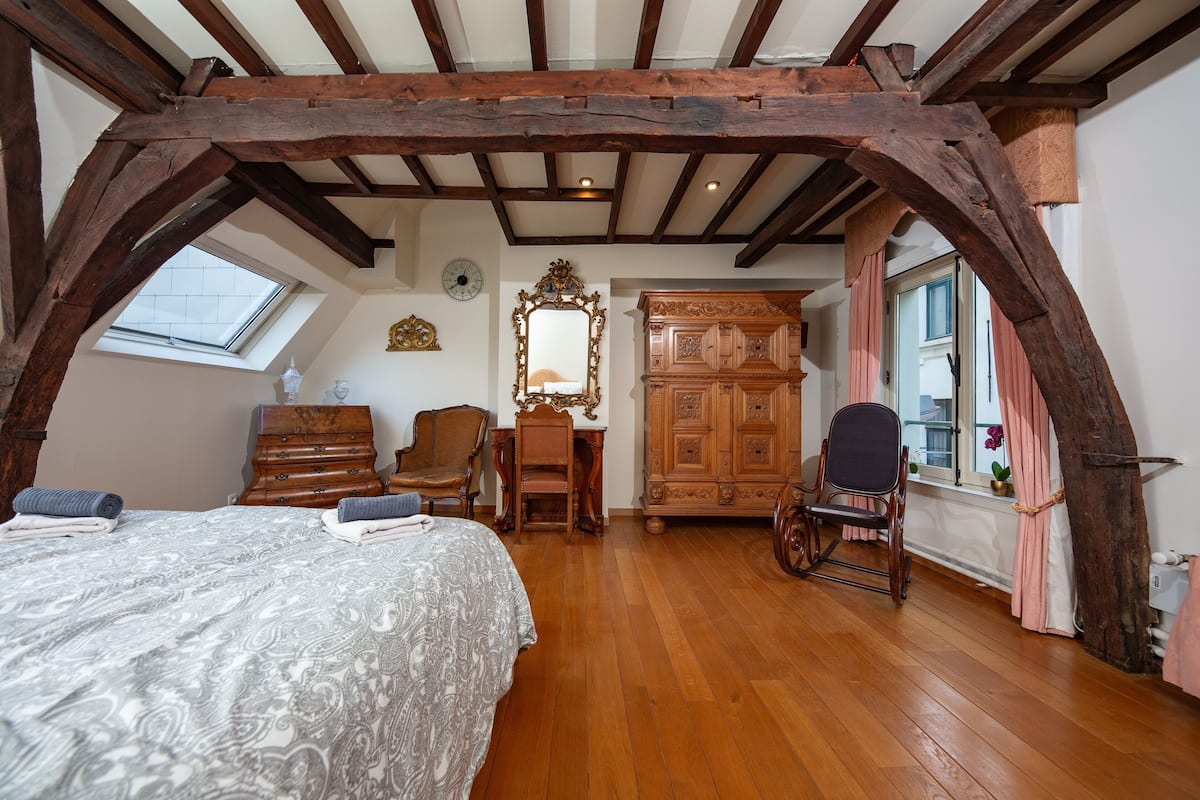A bedroom with a large bed, wooden furniture, a wooden ceiling, and a window.