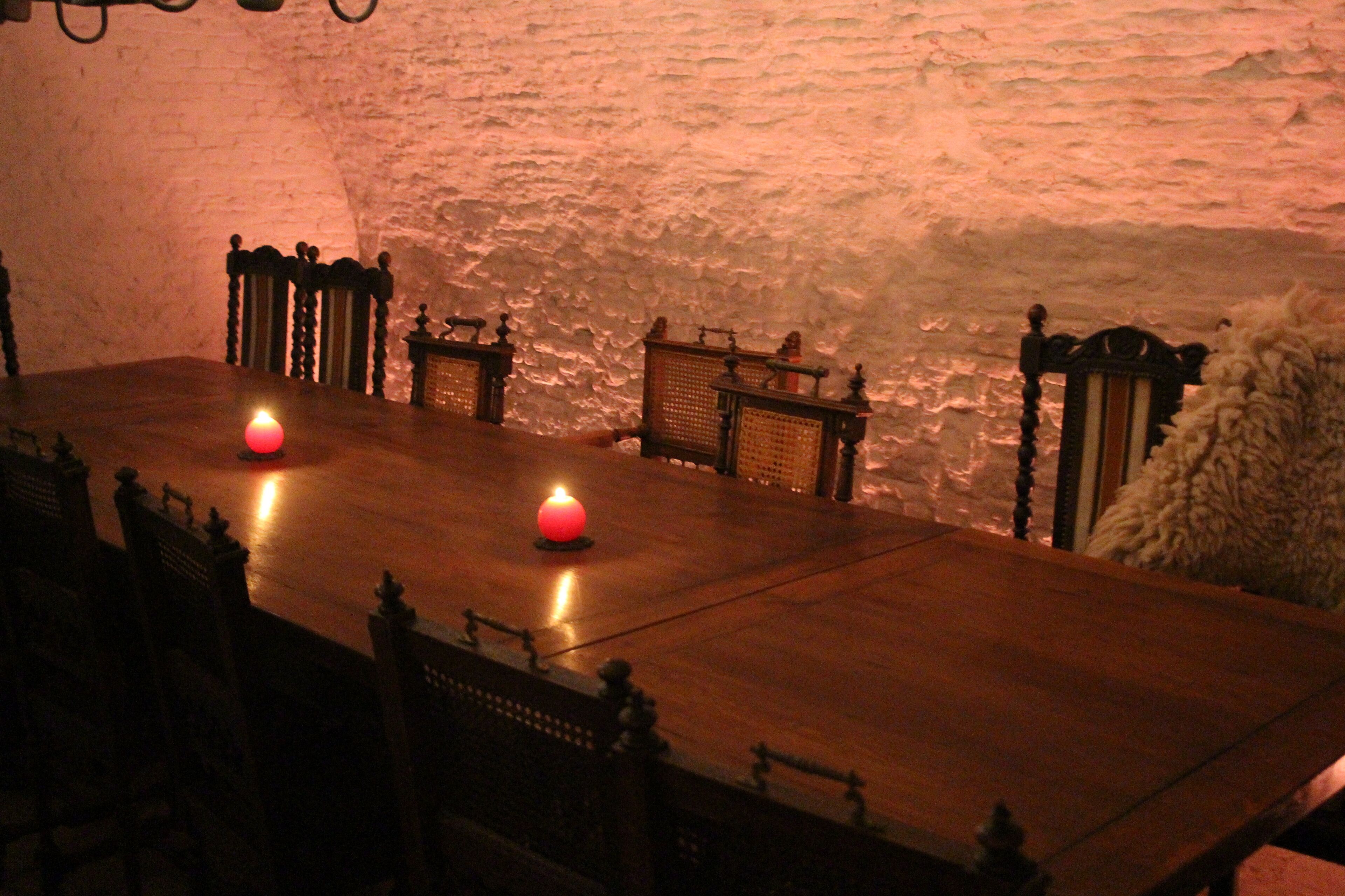 A dining table with candles, wooden chairs, and a stone wall in the background.