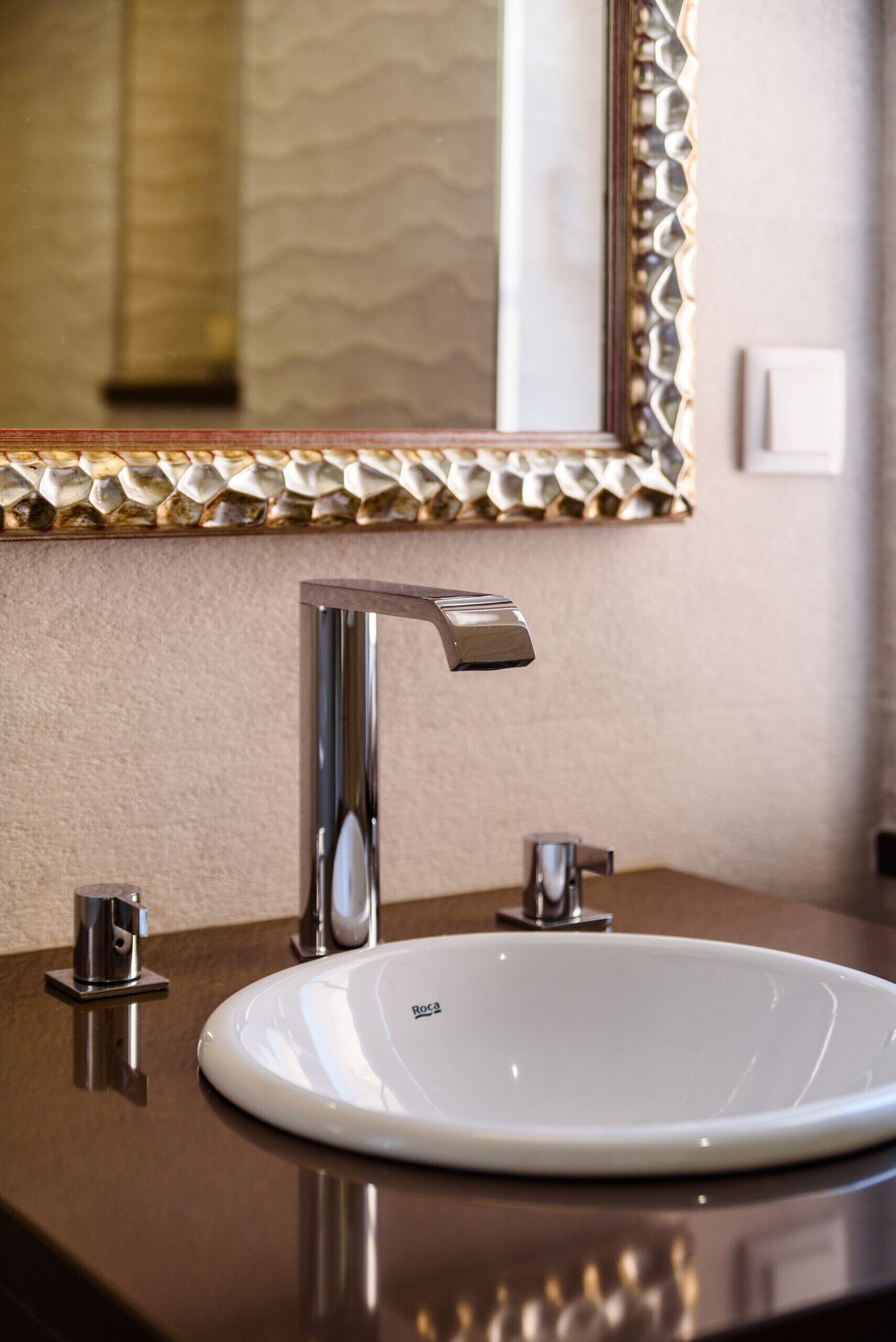 A bathroom with a white sink, a chrome faucet, and a decorative mirror with a textured frame.