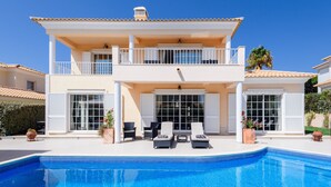 A two-story house with a swimming pool, outdoor seating, and a garden.
