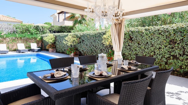 An outdoor dining area with wicker furniture, a pool, and a hedge wall.