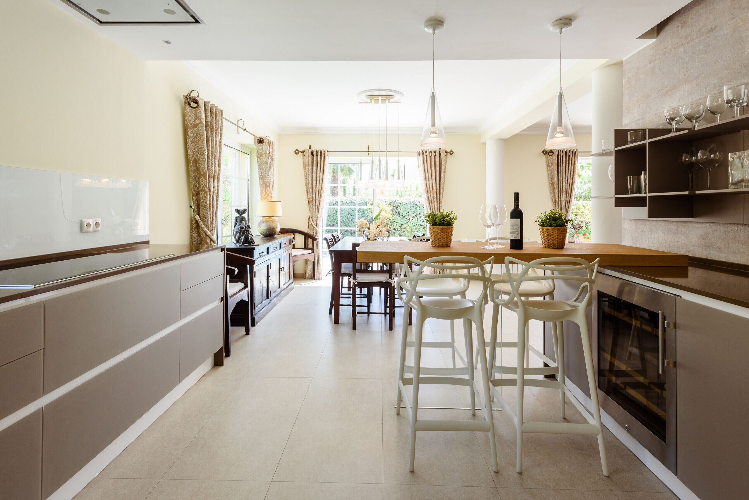 A modern kitchen with a dining area, featuring a central island, bar stools, and a built-in oven.