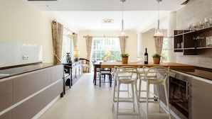 A modern kitchen with a dining area, featuring a central island, bar stools, and a built-in oven.
