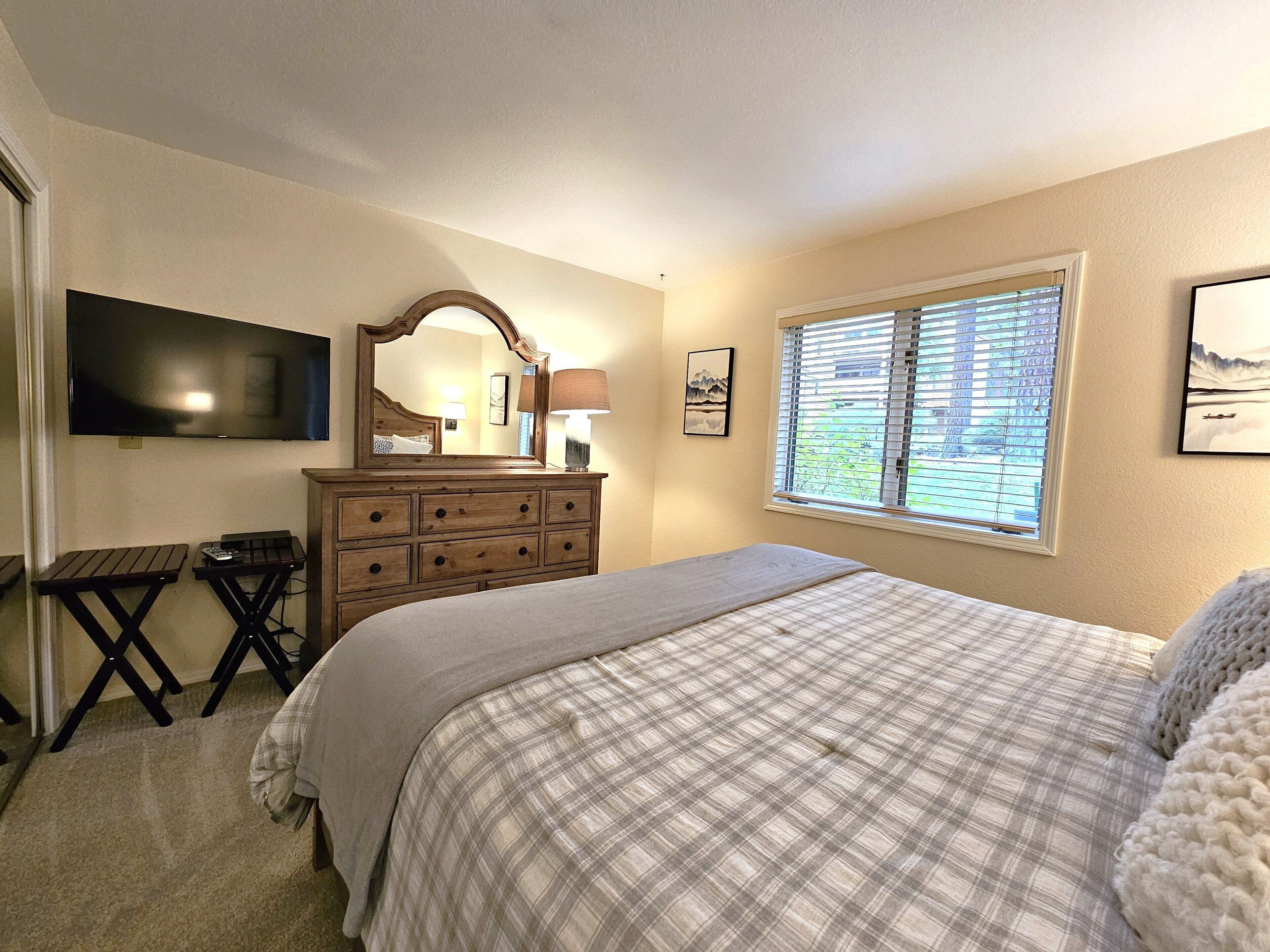 A bedroom with a bed, dresser, TV, window, and artwork.