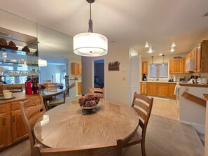 A modern kitchen with wooden cabinets, a round dining table, and a hanging light fixture.