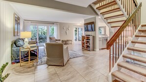 A spacious living area with a staircase, a sofa, a coffee table, and a TV. - Pet Friendly | Luxury Beachwood Townhome | Directly Across the Street from the Beach (Fernandina Beach)