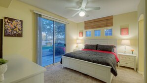 Un dormitorio con cama, ventilador de techo, puerta corrediza de vidrio y mesita de noche con lámpara.