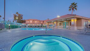 Un área de piscina con varias piscinas, sillones de descanso y un edificio de techo rojo.