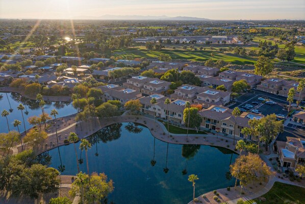 An aerial view of a residential area with a central swimming pool, surrounded by houses and a golf course.