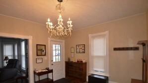 Un salon spacieux agrémenté d’un lustre, d’un banc en bois, d’une porte avec un miroir et d’une bibliothèque.